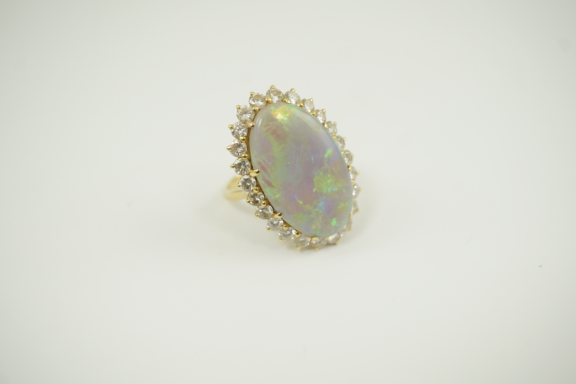 An 18ct gold, white opal and diamond set oval cluster dress ring, the cabochon opal measuring approximately 22mm by 14.5mm, with a depth of 5mm, and bordered by round brilliant cut diamonds, size L, gross weight 6.8 gram